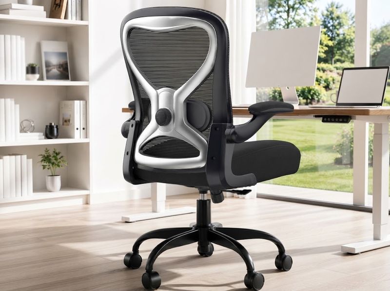 Chair rolled fully under a compact home-office desk, armrests folded vertica